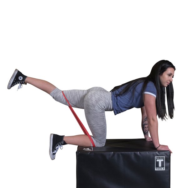 Female athlete on hands and knees on a soft 20x24x30 plyobox, performing leg kickbacks with a red resistance band.