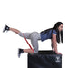 Female athlete on hands and knees on a soft 20x24x30 plyobox, performing leg kickbacks with a red resistance band.