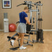 White male in a blue shirt performing a single-leg kickback using the low pulley attachment on the Powerline by Body-Solid P2X Multi-Functional Home Gym.