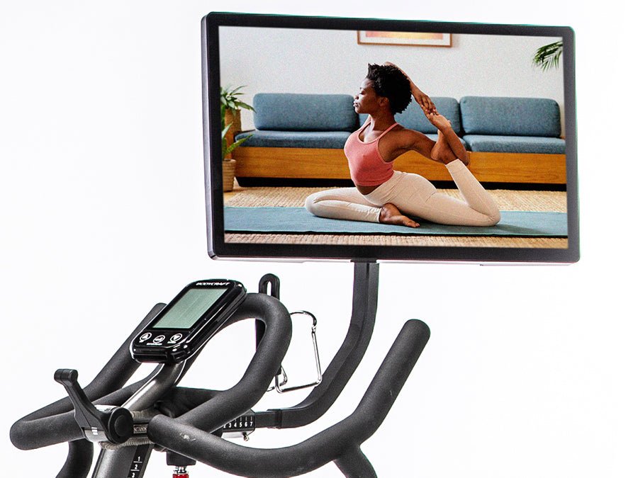 Connect-22 tablet mounted on a BodyCraft bike, displaying a female in a yoga pose on screen while the user follows along with the yoga exercise off the bike