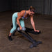 white woman in a teal pants performing bent over one arm rows with metal hex dumbbells on a bench in flat postion