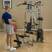 White male in a blue shirt performing bicep curls with a short straight bar attachment from the leg extension low pulley on the Powerline by Body-Solid P2X Multi-Functional Home Gym