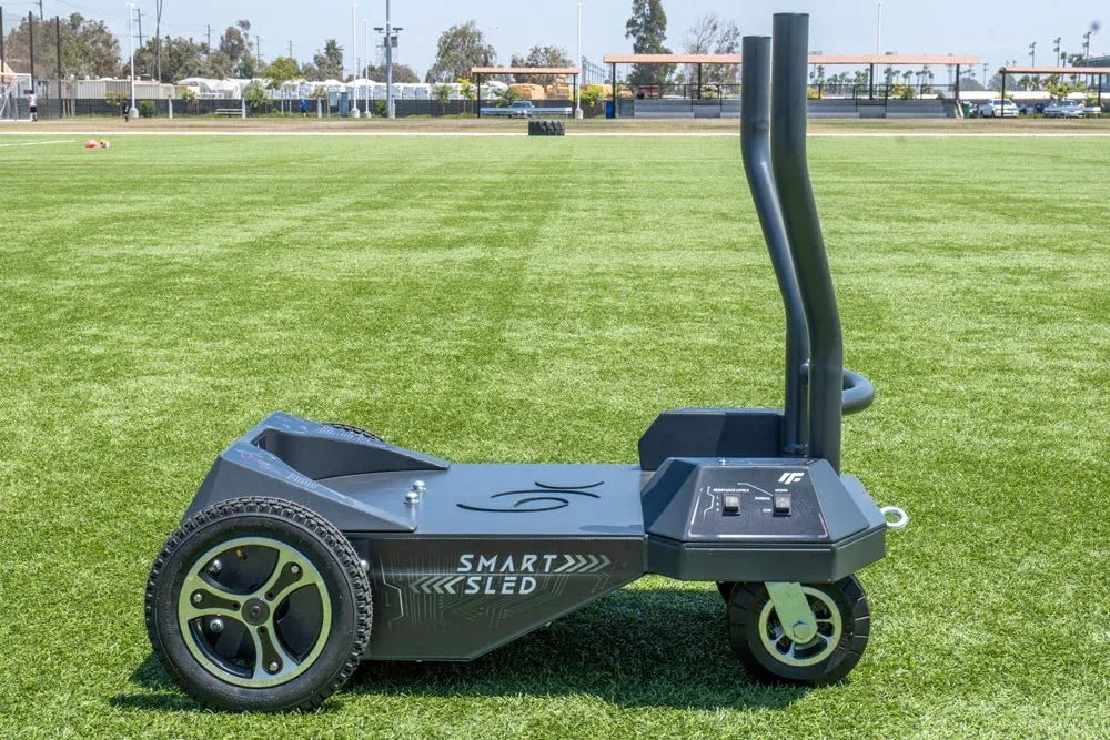 **Alt Text:** Side view of the BodyKore Smart Sled Pro on turf at an athletic field, showcasing its sturdy design and all-terrain wheels, perfect for outdoor training and enhancing athletic performance.