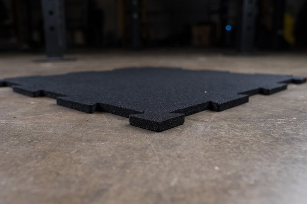 Close-up low to floor of interlocking black puzzle mats made of heavy-duty rubber, showcasing the puzzle-style edges for easy installation, designed to protect floors and equipment in any workout space.